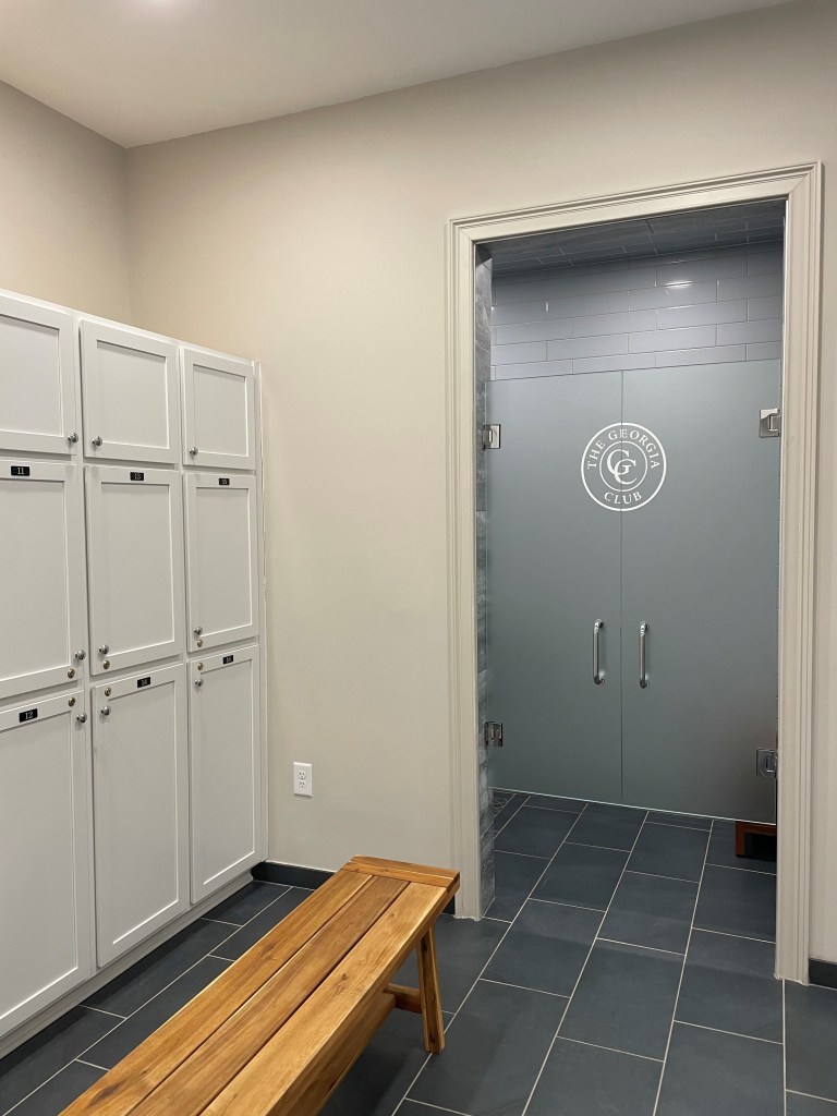 Lockers to the left and the entrance to the showers with The Georgia Club's logo etched onto the transparent door.